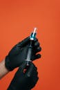 在橙色背景下，一只戴着黑色手套的手准备注射器的特写