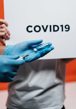 Healthcare worker with syringe and vaccine highlighted by COVID-19 sign.