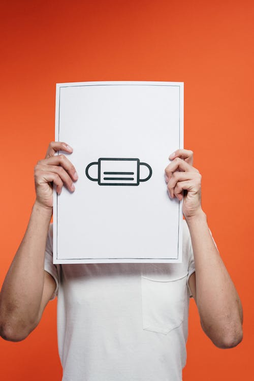 Free Person Holding White Paper With A Drawing Of Face Mask Stock Photo