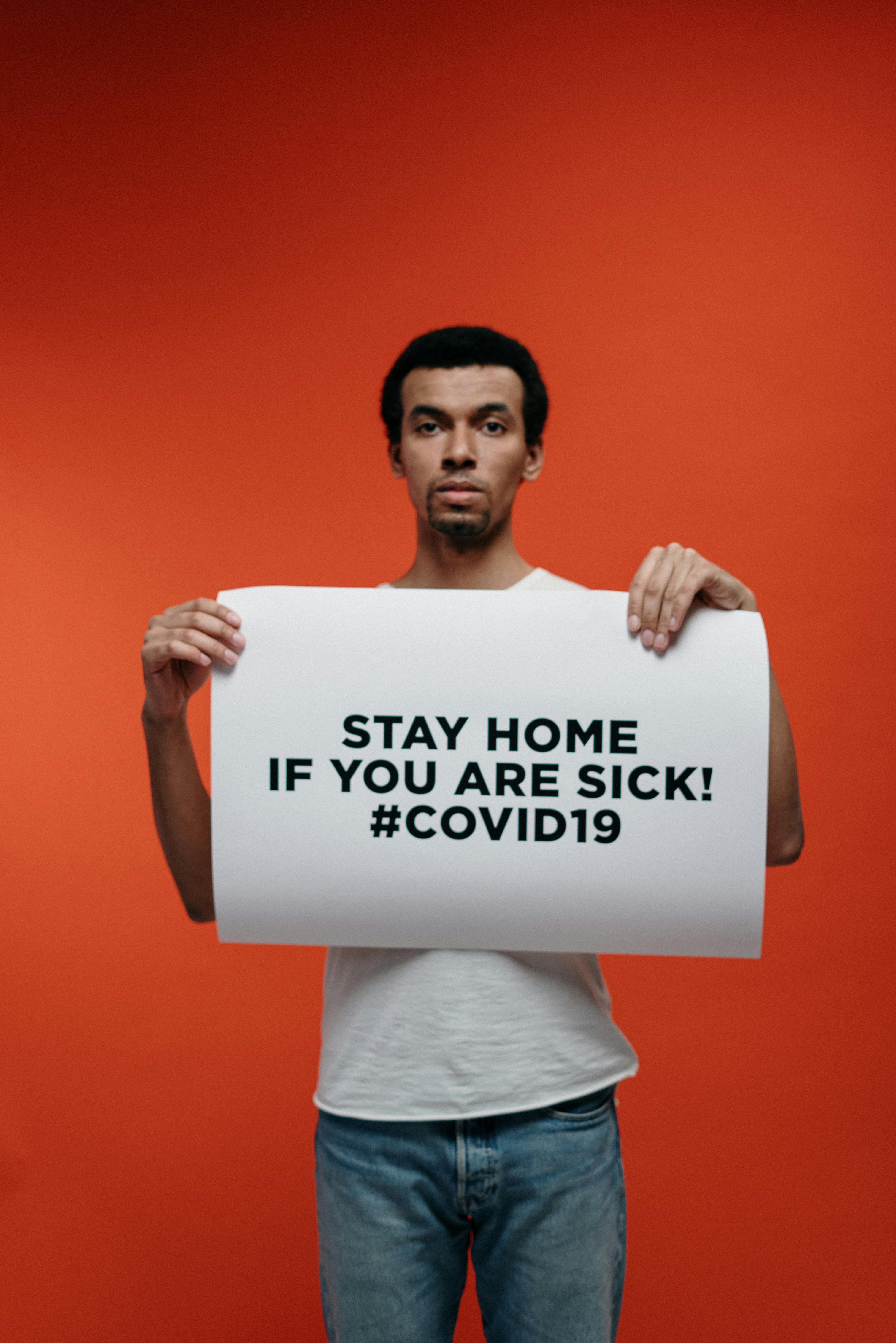 man in white crew neck t shirt holding stay at home sign