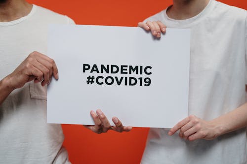 Free Two people holding a poster with 'Pandemic #COVID19' message on a vibrant background. Stock Photo