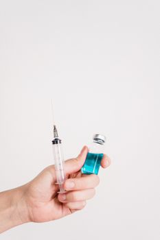 白色背景下，一只手拿着疫苗注射器和瓶子