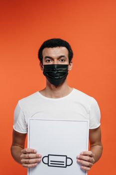 一名戴着口罩的男子举着亮橙色背景的口罩安全标志