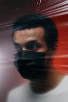 Portrait of a man wearing a mask behind a blurred surface, depicting isolation and protection.