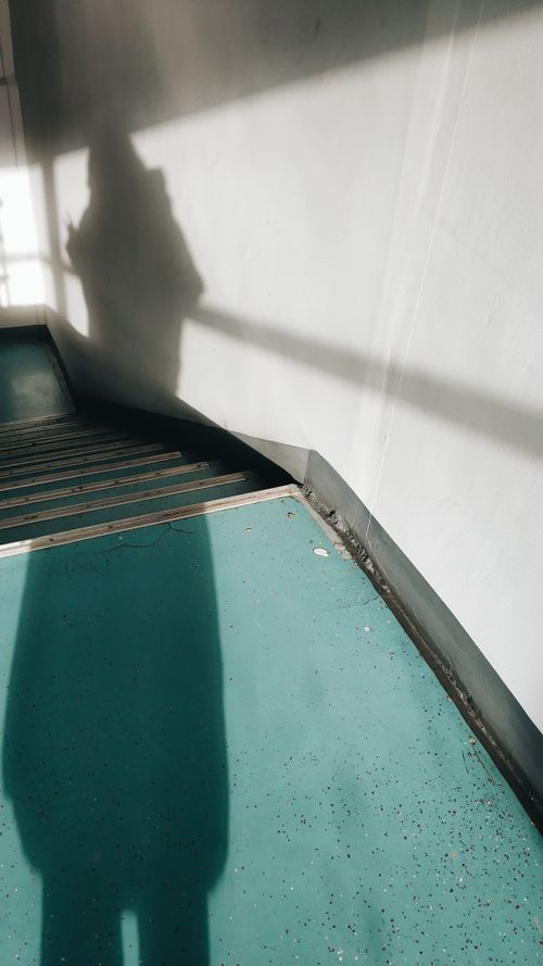 Free Shadow cast on a teal staircase in a well-lit indoor space, capturing abstract forms. Stock Photo