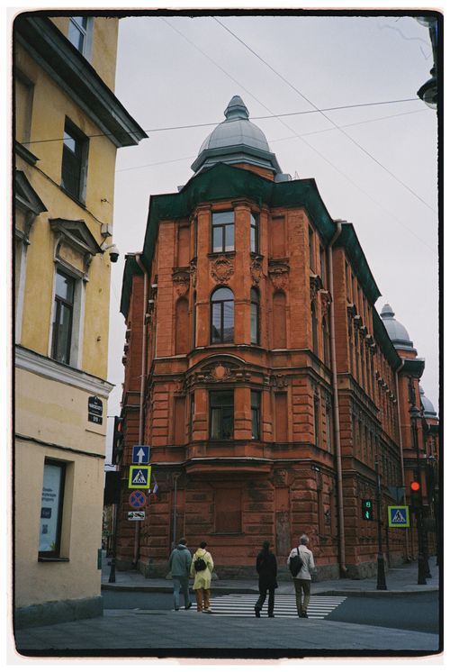 Free A red brick building with unique architecture on a city street with pedestrians crossing. Stock Photo