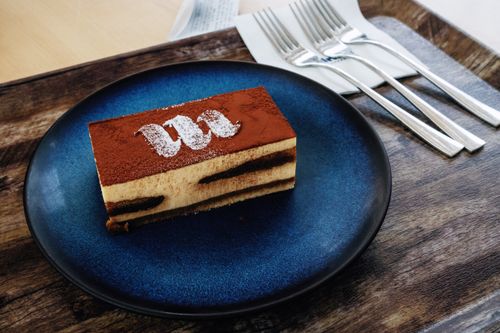 Free Close-up of a tiramisu slice with cocoa topping on a blue plate, styled with cutlery. Stock Photo