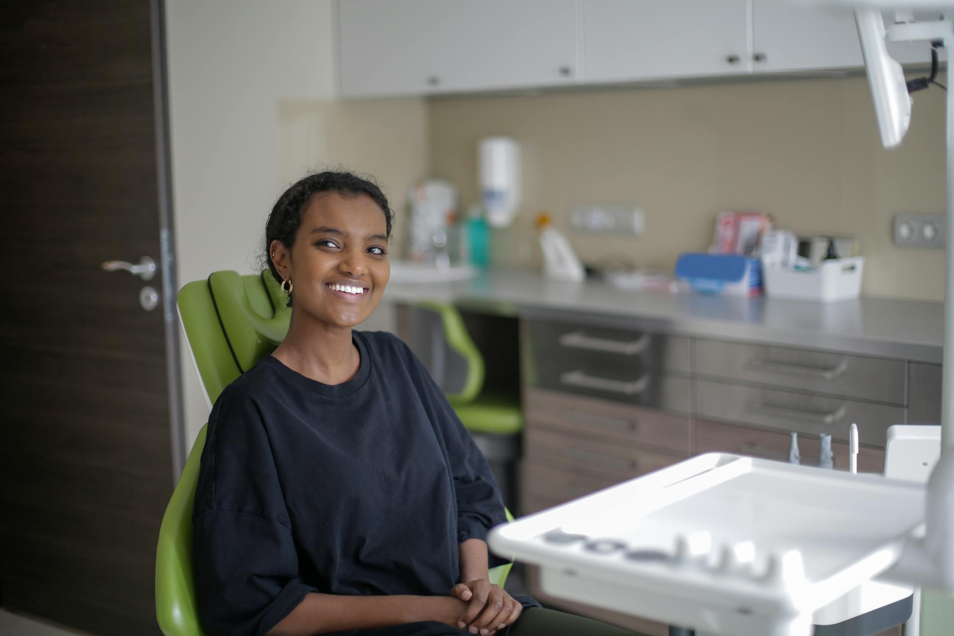 Cheerful African American woman sitting on dental chair in clinic