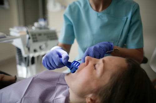 Free Crop anonymous female dentist in sterile gloves and uniform putting plastic dental impression in lying patients mouth in clinic in afternoon Stock Photo