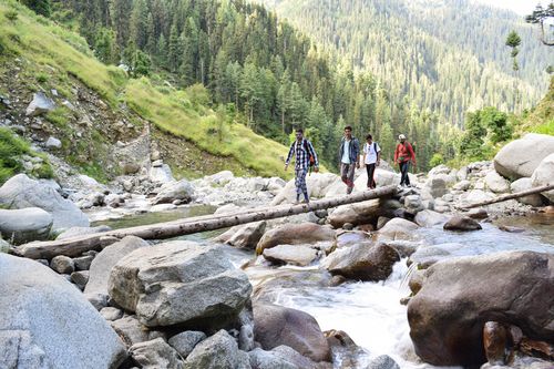 Free Adventurers cross a wooden bridge over a serene stream in Chail, surrounded by lush greenery. Stock Photo