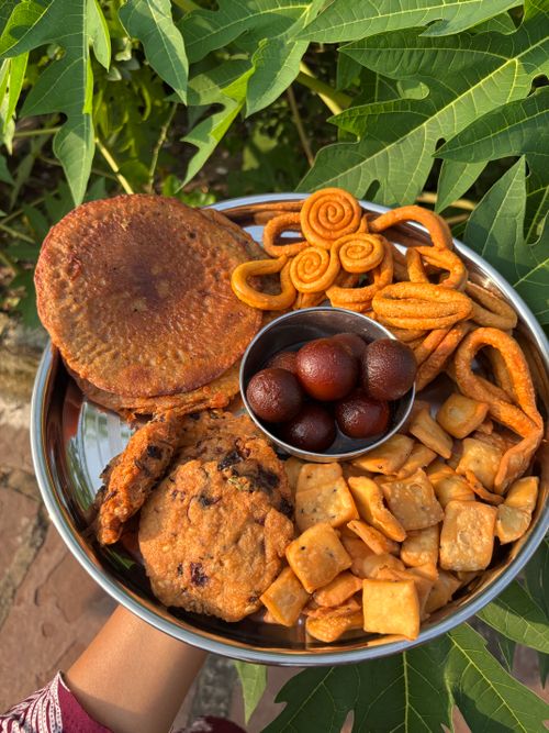 Free A vibrant display of Indian sweets and snacks served on a metal plate outdoors. Stock Photo