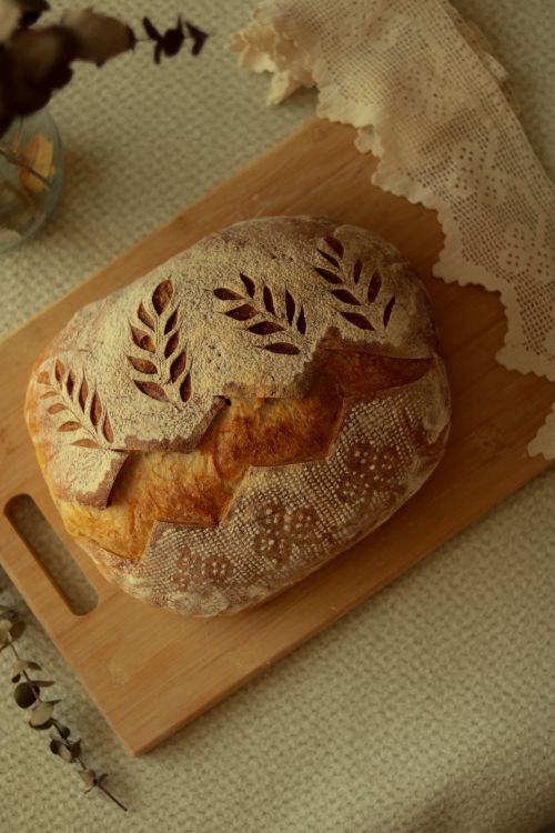 Free Delicately scored artisan sourdough bread placed on a wooden board, exuding a rustic, homely feel. Stock Photo