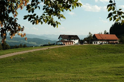 Free Idyllic countryside view of a farmhouse on green hills with distant mountain backdrop under a clear sky. Stock Photo
