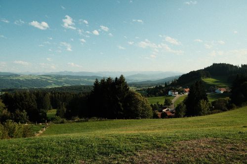 Free Picturesque view of the countryside with rolling hills, lush greenery, and distant mountains under a clear sky. Stock Photo
