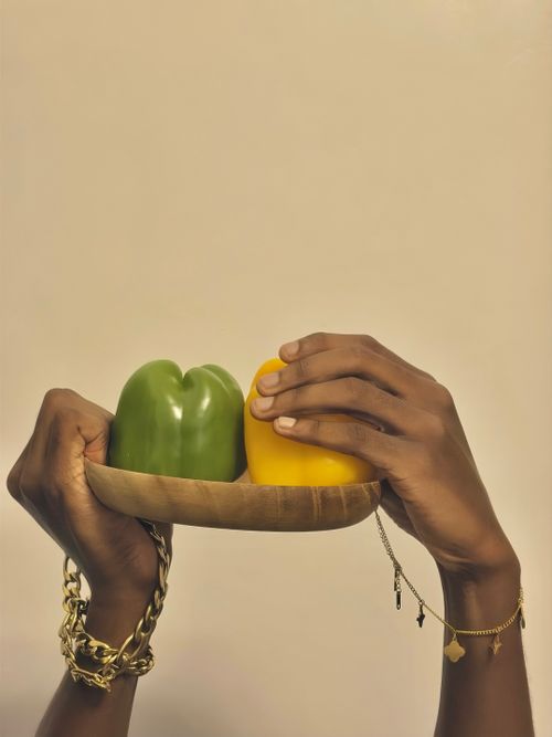 Free Close-up of hands with jewelry holding green and yellow bell peppers on a wooden plate. Stock Photo