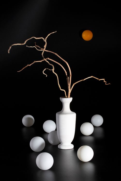 Free Elegant still life of a white vase with branches and scattered spheres on black background. Stock Photo