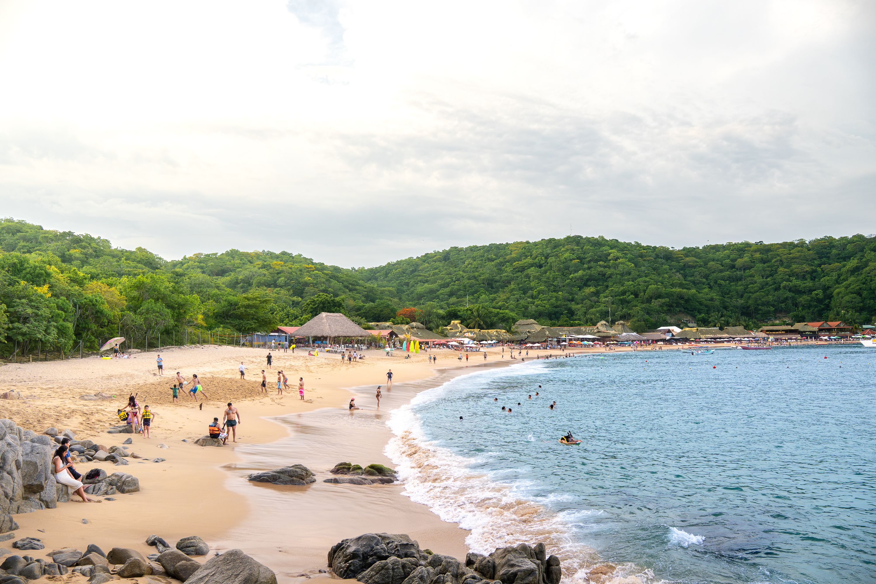 A bustling beach scene with people enjoying the sun and sea at Santa María Huatulco, Oaxaca, México.
