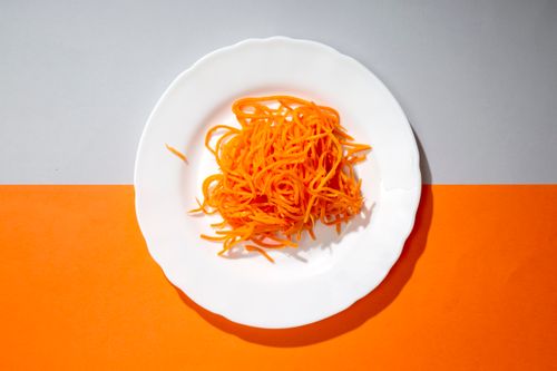 Free Bright photo of spiralized carrot on a white plate against an orange and gray background. Stock Photo