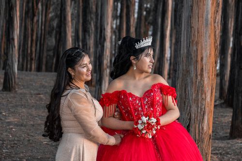 Free Young woman in red quinceañera gown, with mother, surrounded by forest trees. Stock Photo