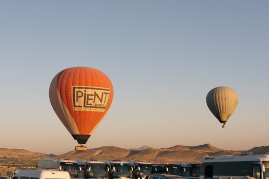Hot air balloons soar above the scenic landscape of Cappadocia, Türkiye at sunrise.