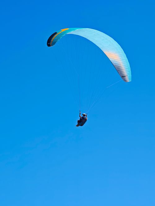 Free Lone paraglider soaring gracefully through a bright blue sky, capturing the essence of freedom and adventure. Stock Photo