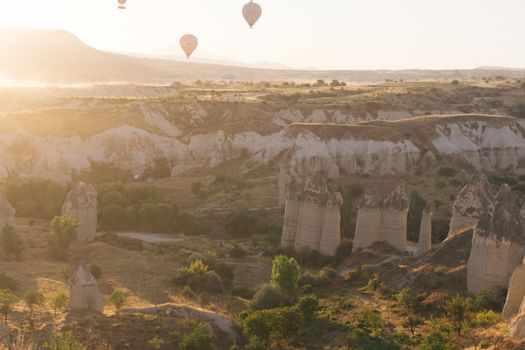 Scenic view of hot air balloons soaring above Cappadocia's rugged terrain at sunrise.