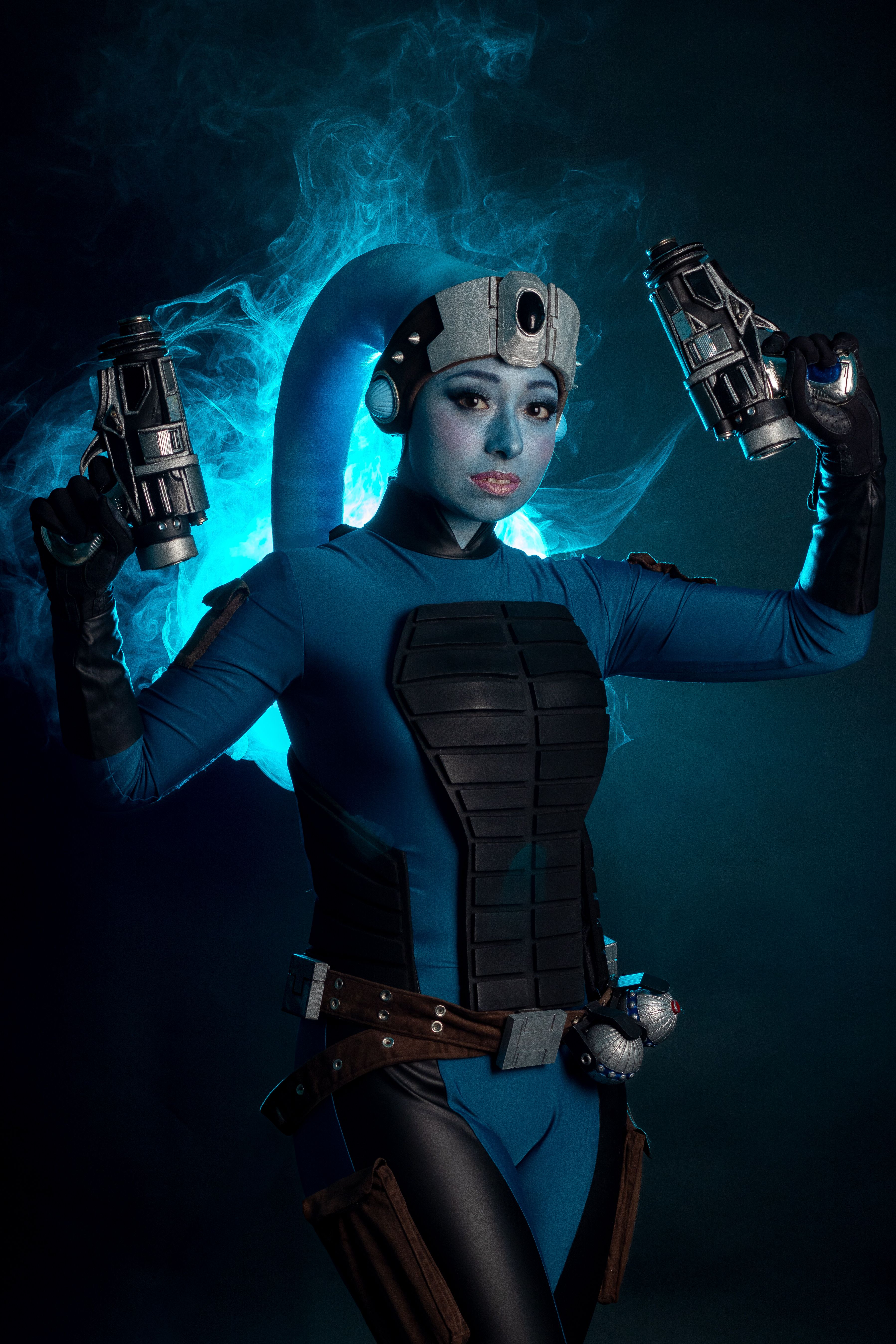 Cosplay character in detailed futuristic armor posing with dual blasters against a smoky backdrop.