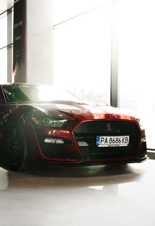 Free Elegant red sports car bathed in sunlight in a sleek indoor showroom setting. Stock Photo