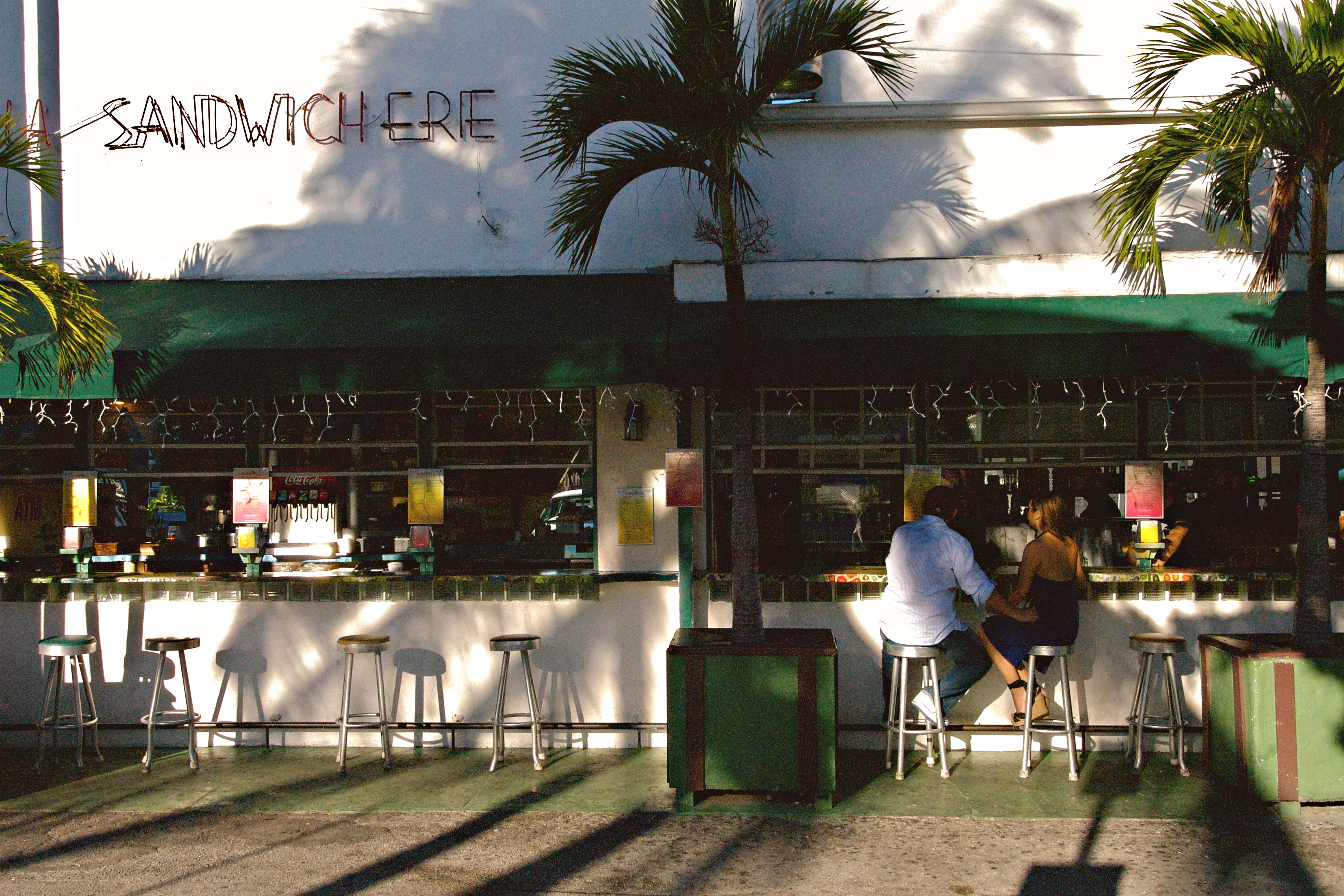 A couple sitting at an outdoor cafe counter in Miami Beach, Florida, enjoying a sunny day.