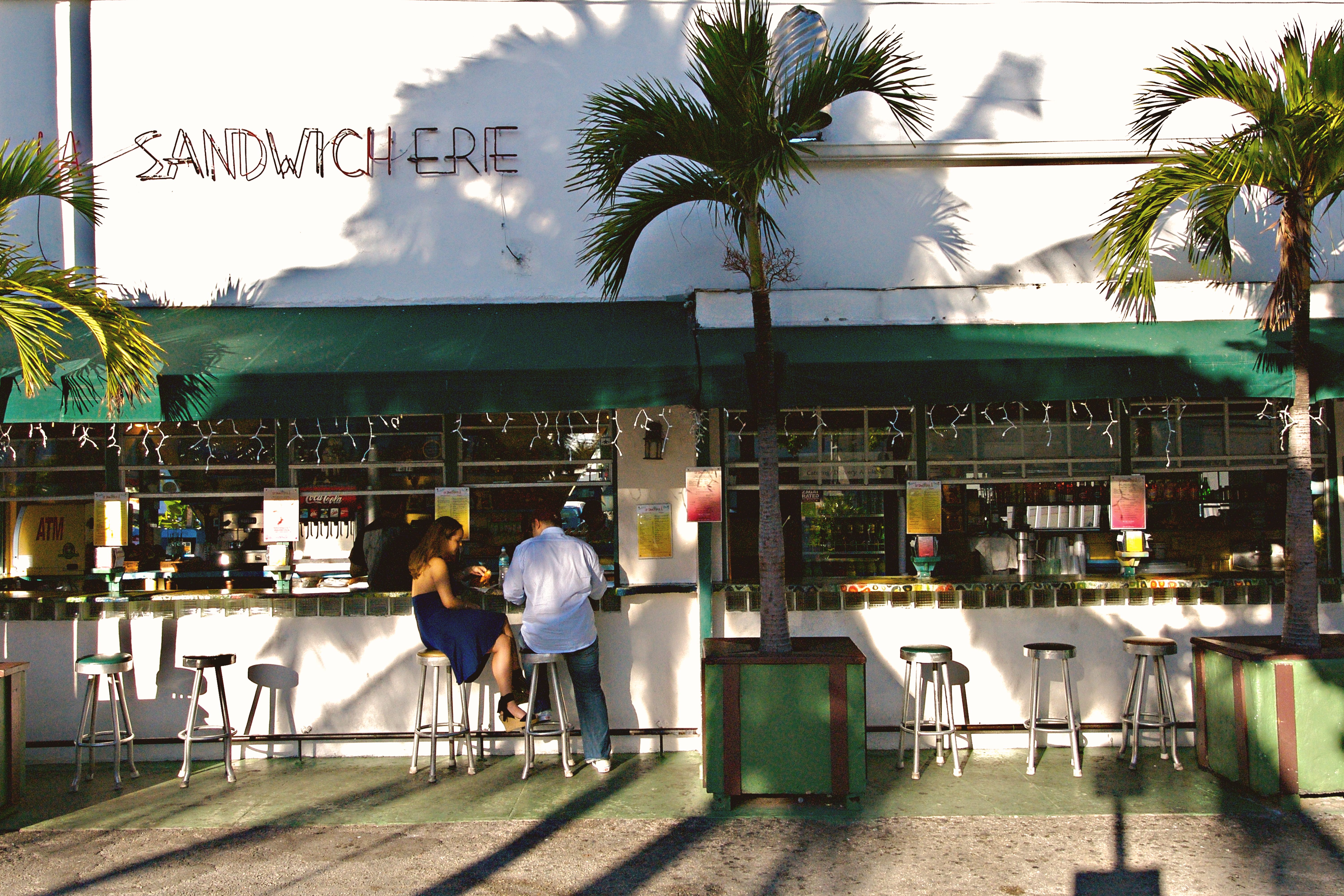 Charming outdoor sandwich café in Miami Beach with palm trees and vibrant atmosphere.