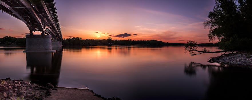宁静的日落倒映在平静的河面上，映出桥梁和树木的剪影