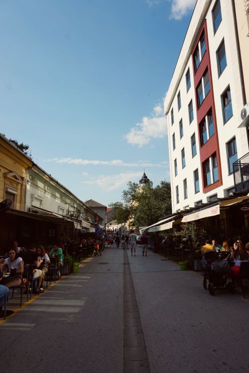Free Sunny day on a bustling street in Novi Sad with cafes and people enjoying outdoors. Stock Photo