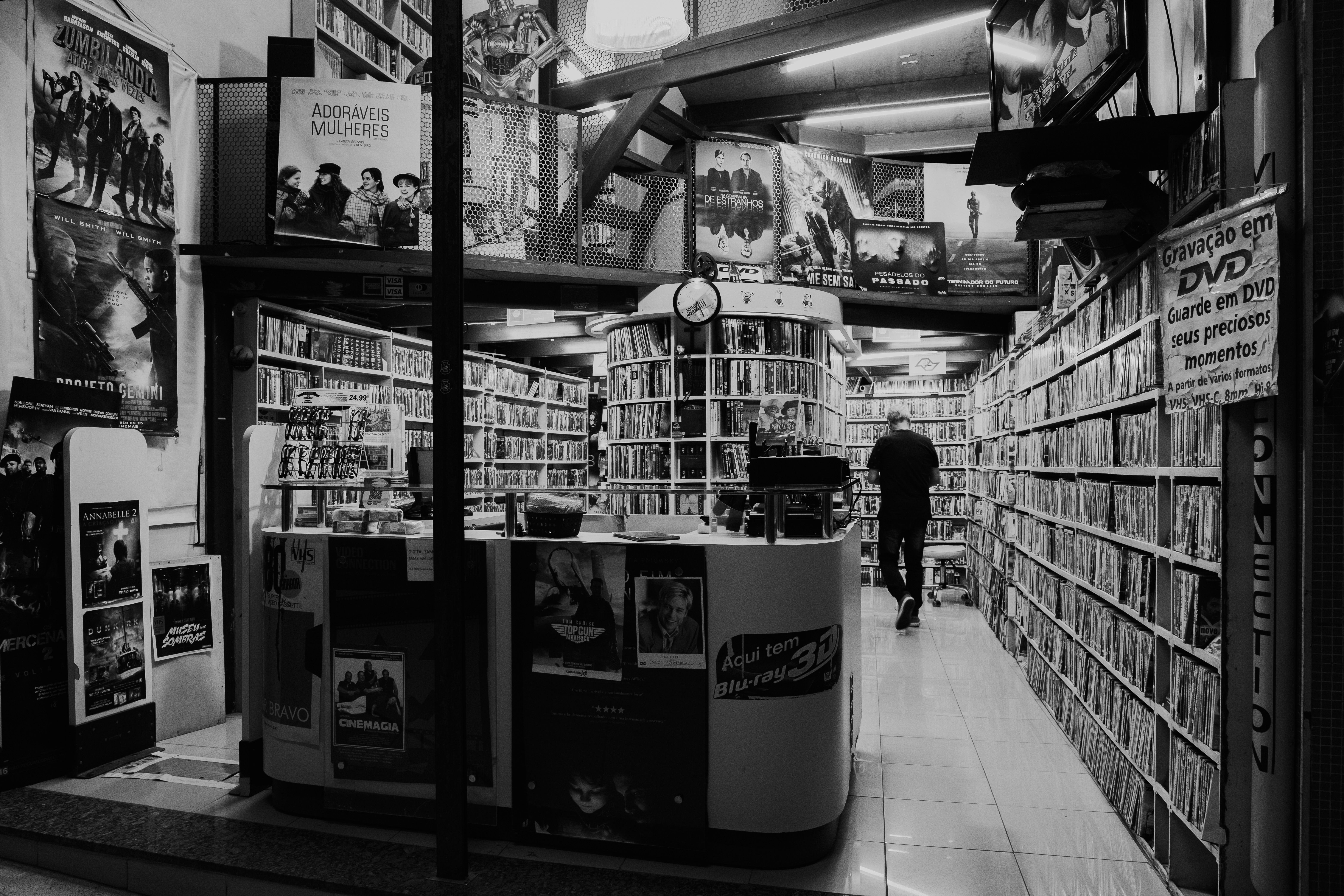 Monochrome view of a DVD store interior with a person browsing the shelves.