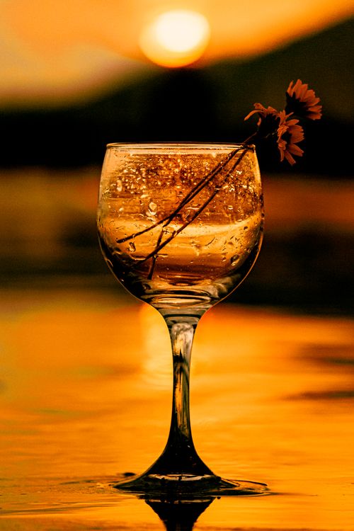 Free A wine glass with dew drops and flowers against a vibrant sunset backdrop, creating a romantic ambiance. Stock Photo