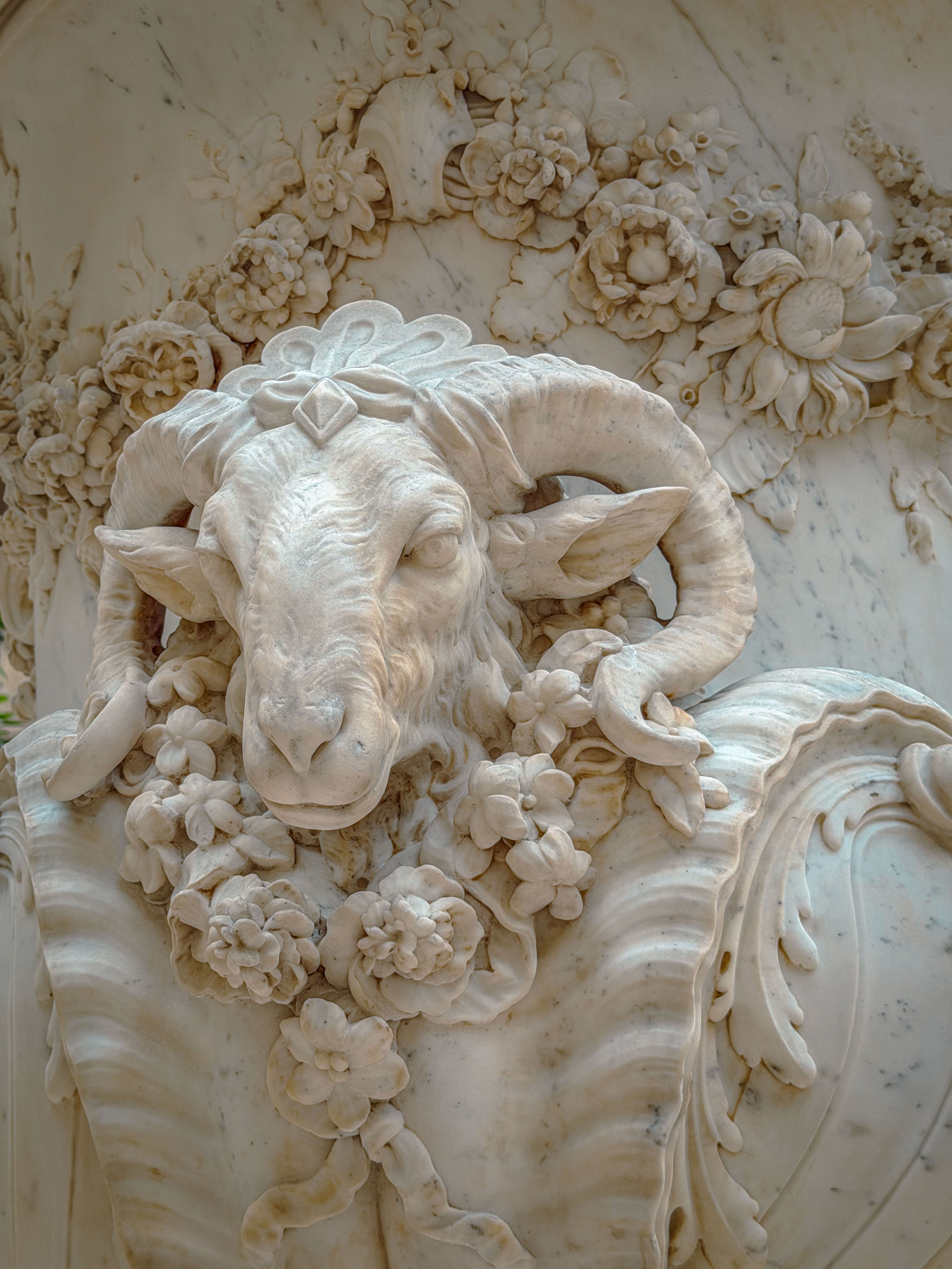 Detailed marble sculpture featuring a ram's head adorned with floral carvings, showcasing exquisite craftsmanship.