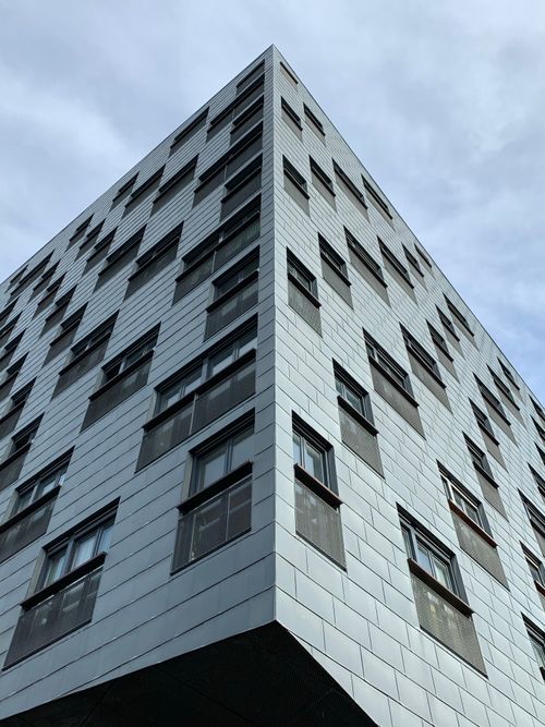 Free Low angle view of a modern building facade with grid pattern windows under a cloudy sky. Stock Photo