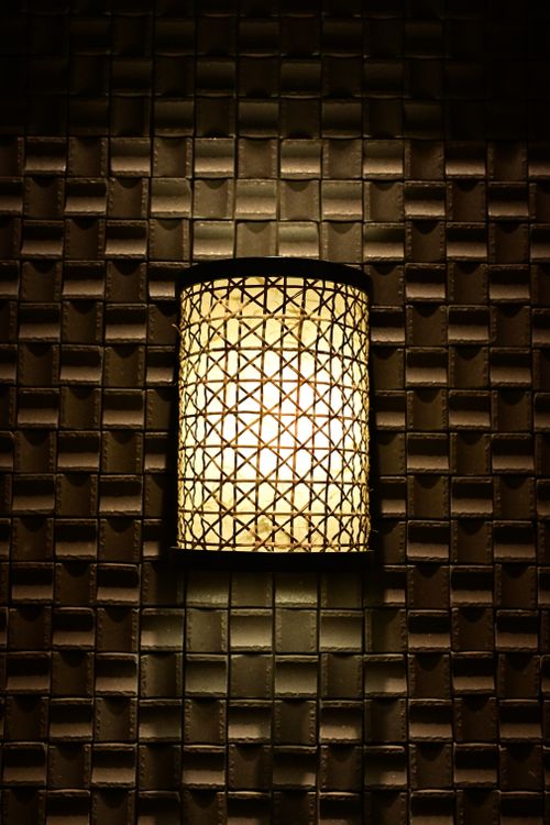 Free A warm glowing wall light with a woven design, set against a textured tile background, creating ambient lighting. Stock Photo