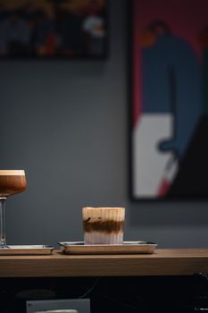 A minimalist cafe scene featuring layered coffee drinks on a wooden counter with soft lighting.