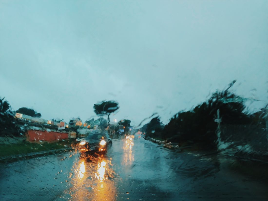 Blurry view of rainy road through windshield with vehicle lights and reflections