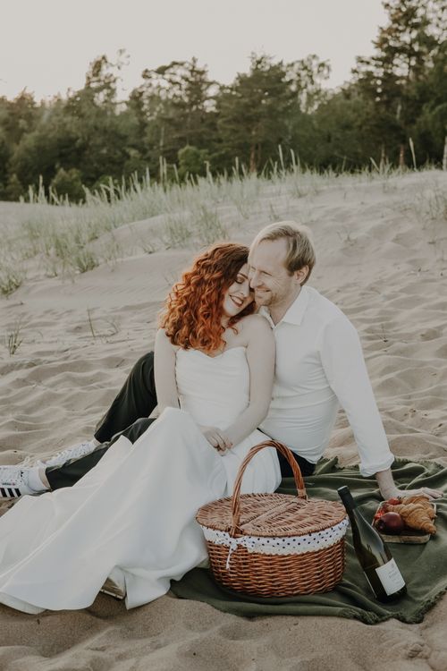 Free Couple enjoying an intimate beach wedding picnic at sunset with wine and basket. Stock Photo