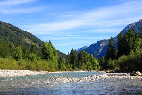 Free Clear mountain river flowing through forested valley under a bright summer sky. Stock Photo