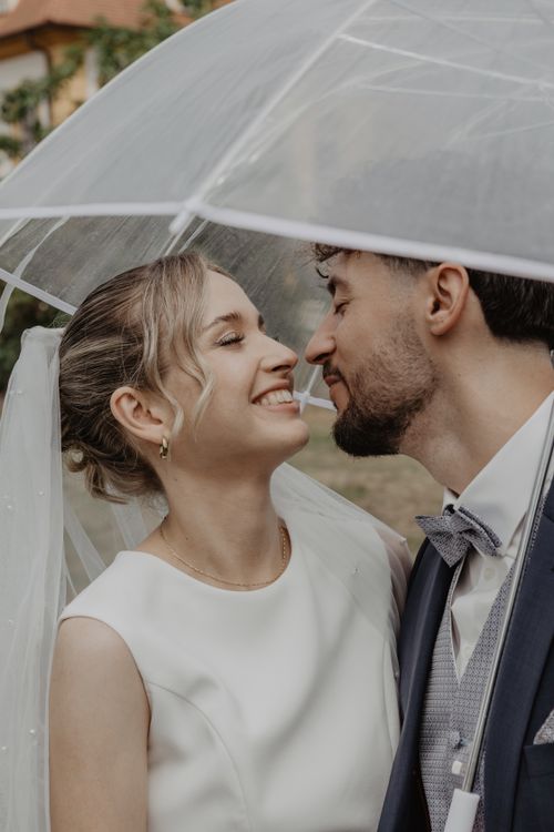 Free A joyful couple on their wedding day, sharing a moment under a clear umbrella. Stock Photo