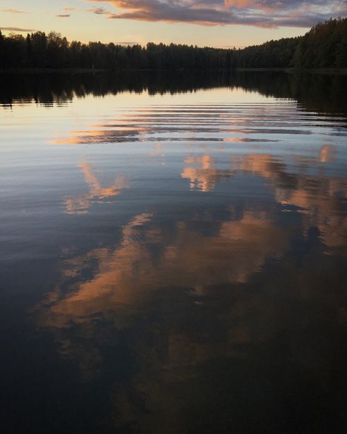 Free Capture of a serene sunset reflecting on a tranquil lake surrounded by trees, creating a peaceful atmosphere. Stock Photo
