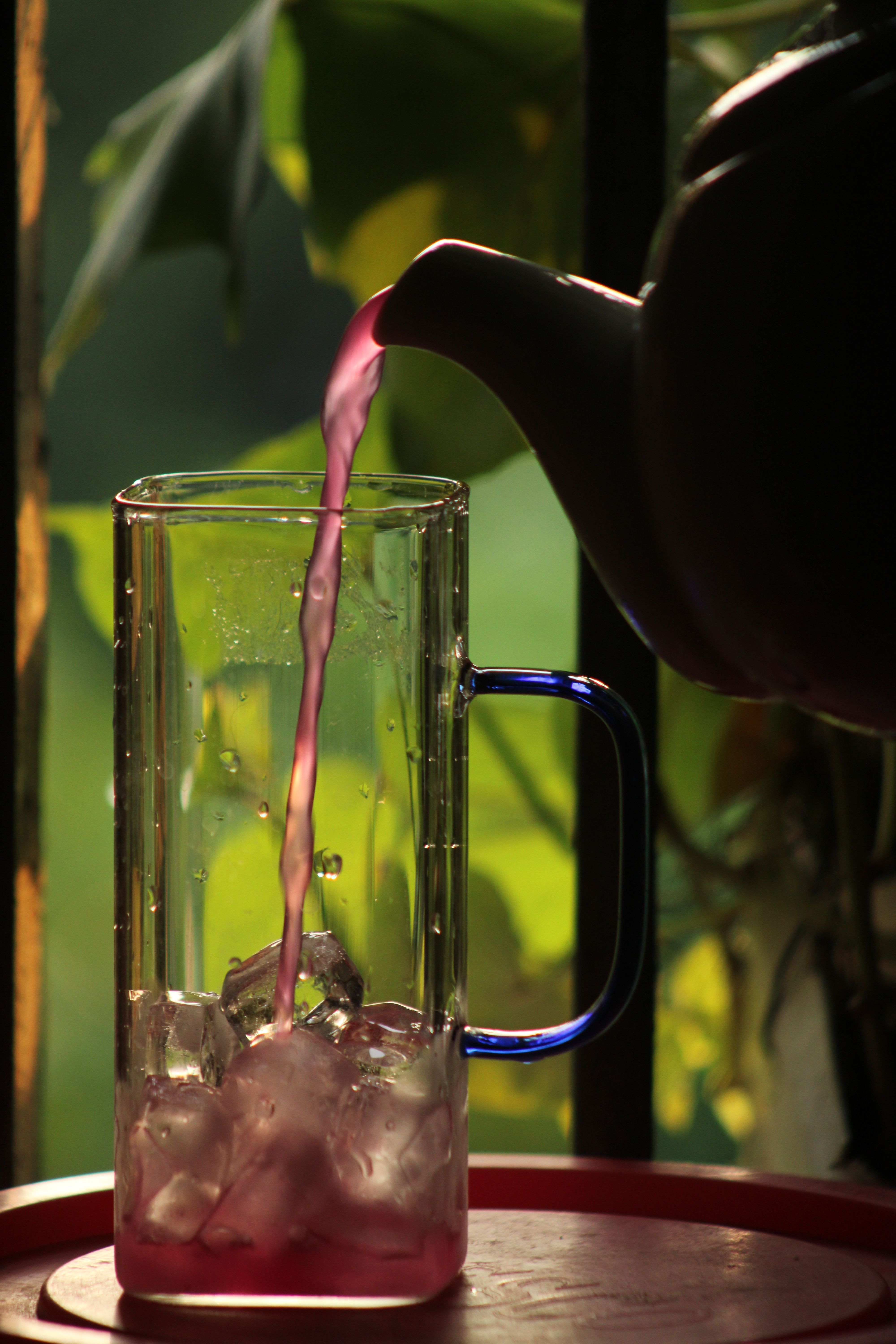 A vibrant pink drink is poured into a glass of ice in a lush setting.