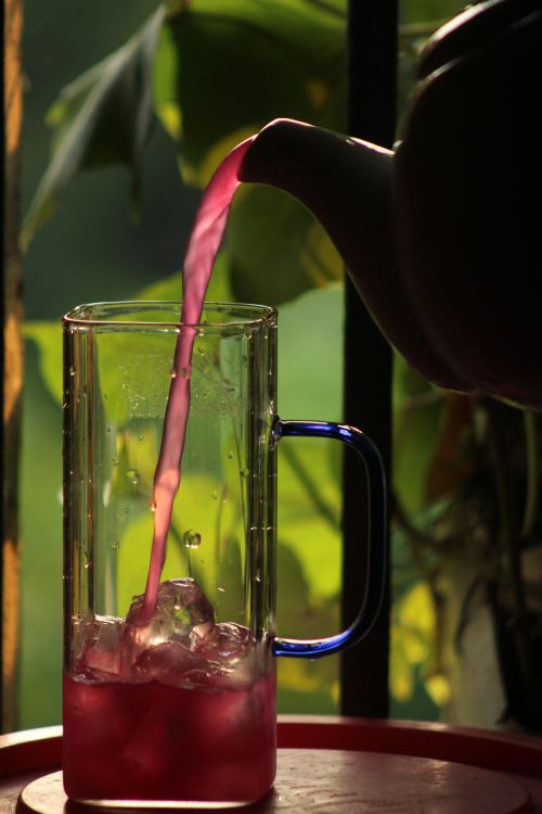 Free Refreshing pink beverage pouring into glass with ice, backlit by sunlight. Stock Photo