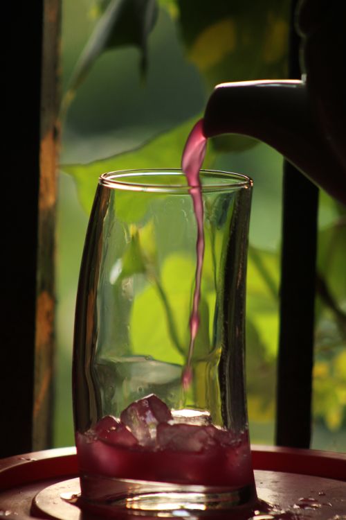 Free Lavender iced tea being poured into a glass with ice on a warm day, creating a refreshing scene. Stock Photo