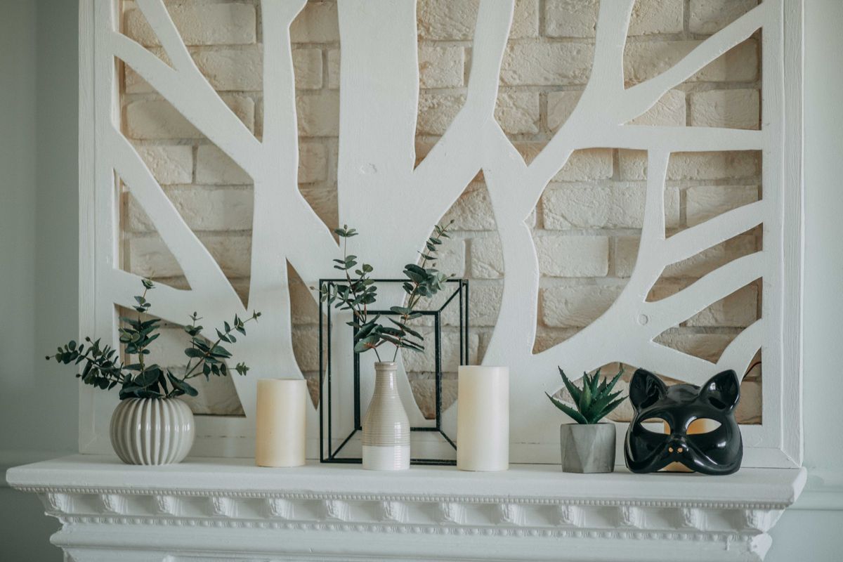 A stylish mantel display featuring candles, vases, plants, and a decorative mask against a modern backdrop. Stock Photo.