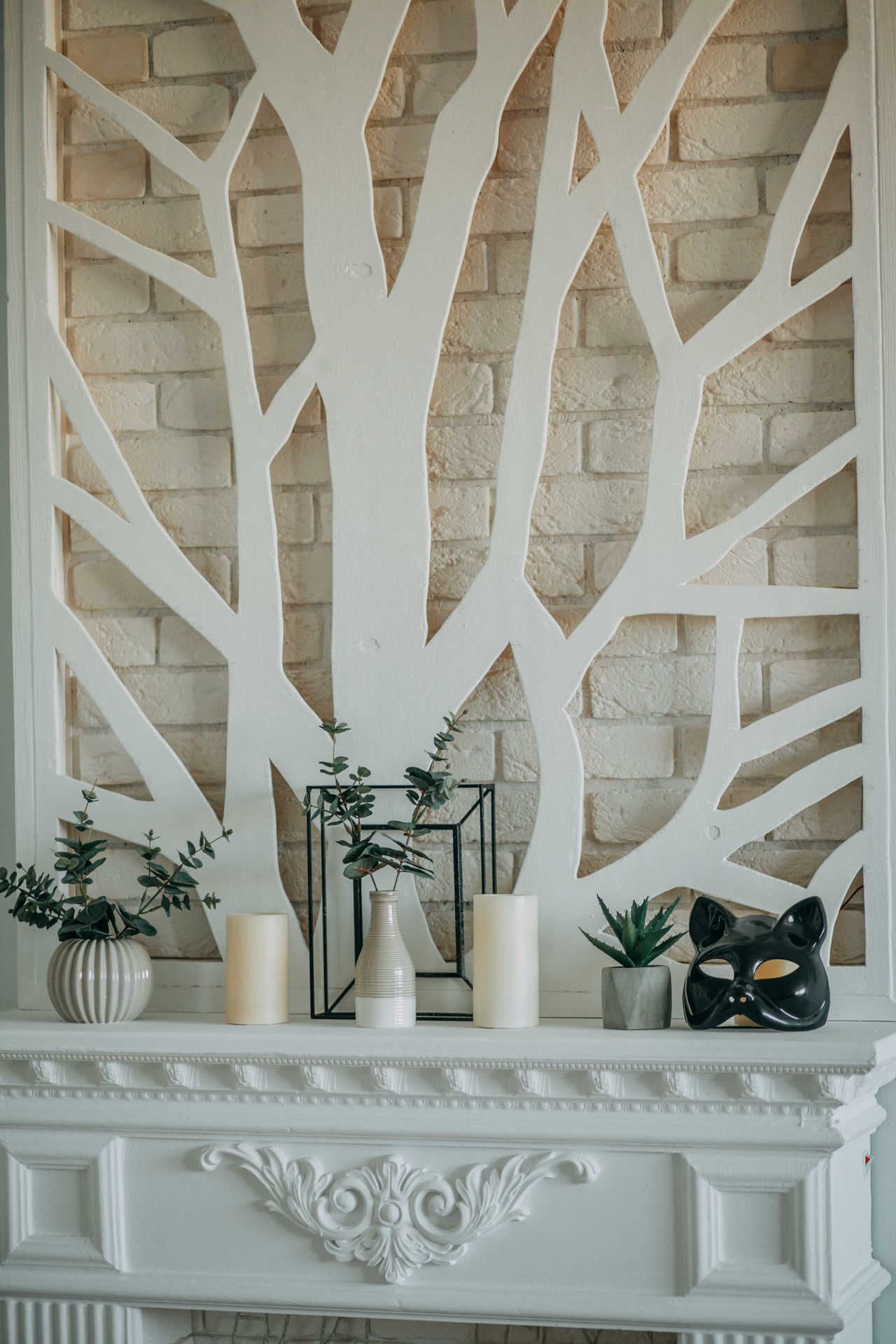 Two cream candles styled on a white mantel with vases, plants and a black cat mask