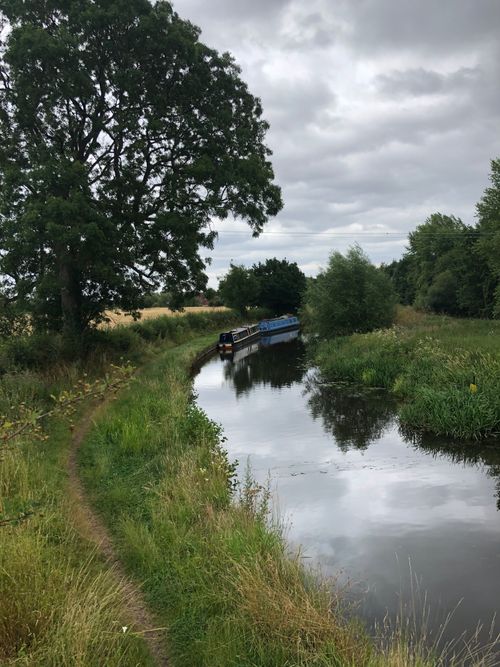 Free Calm river scene with a narrowboat navigating lush greenery on a cloudy day in England. Stock Photo
