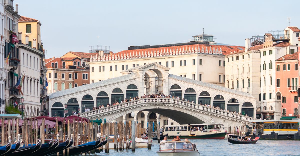 Iconic view of Rialto Bridge with bustling boats on the Grand Canal in Venice, Italy.